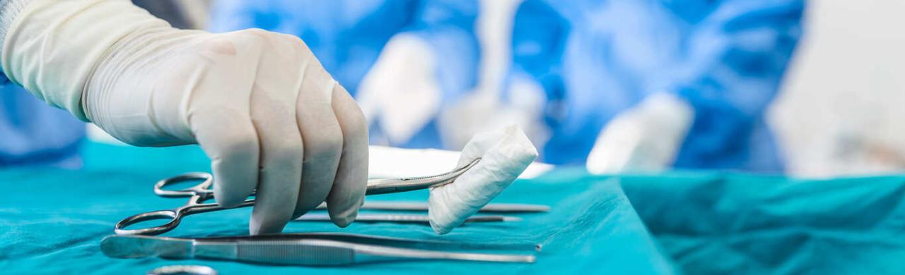 Infirmier de bloc opératoire saisit une compresse à l'aide d'une paire de ciseaux pour l'opération d'un patient